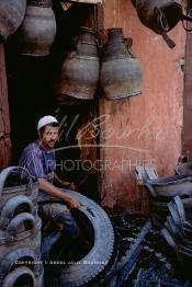 Image du Maroc Professionnelle de  Un Homme découpe un pneu de camion pour le transformer  en différents objets dont quelques uns sont accrochés au dessus. Plusieurs ateliers existaient dans rue situés derrière le cinéma Mabrouka où quelques artisans transformaient des pneus usagés en sceau pour hammam, cruche ou jarre que les paysans utilisaient pour faire sortir l’eau des puits. A cette époque le recyclage des pneus faisait partie intégrante du paysage social au Maroc, presque tous les hammams ont utilisés ces sceaux en caoutchouc à la place de ceux en bois, à cause de leur prix exorbitant et surtout qui se brisaient souvent par les lancements des ouvriers aux heures du nettoyage, Mercredi 18 Mai 1988. (Photo / Abdeljalil Bounhar)